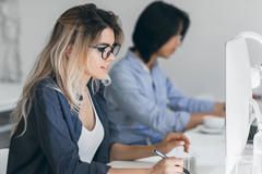 Busy female freelancer with long hair working with tablet and drinking coffee